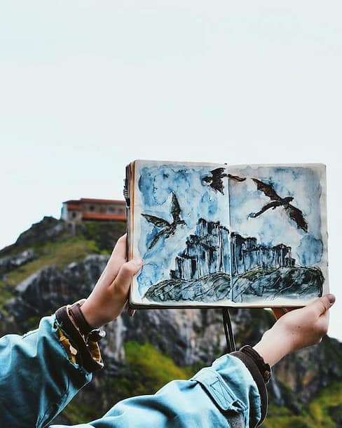 beautiful dragon watercolor drawing held by hands with a mountain behind it