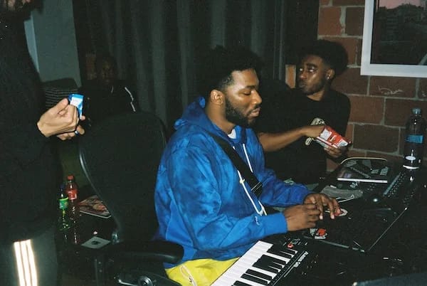 music producer in the studio with a man at the keyboard and another man behind him