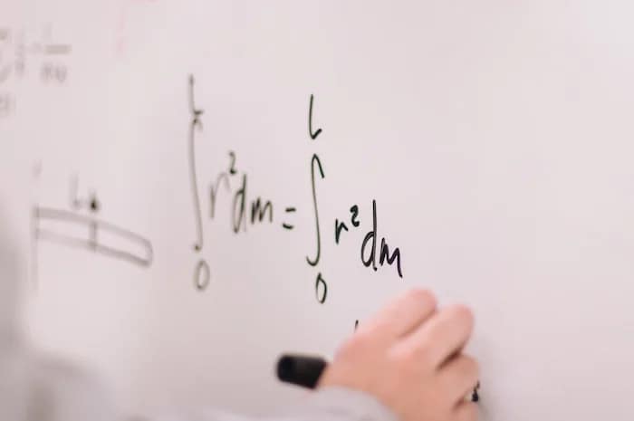 a math formula on a whiteboard with a hand writing it