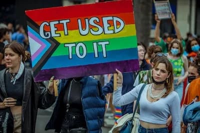 LGBTQ+ Trans person holding a get used to it poster at a pride parade