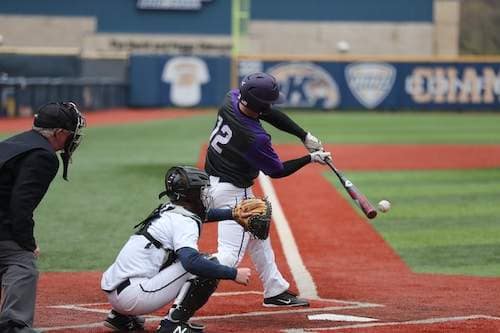 right handed High school batter hitting the ball while up at the plate with umpire and catcher behind him