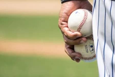 hand holding two major league baseballs with pinstriped pants